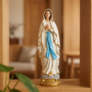 Statue de la Vierge Marie en résine blanche robe aux bordures dorées et écharpe bleue mains jointes posée sur étagère en bois