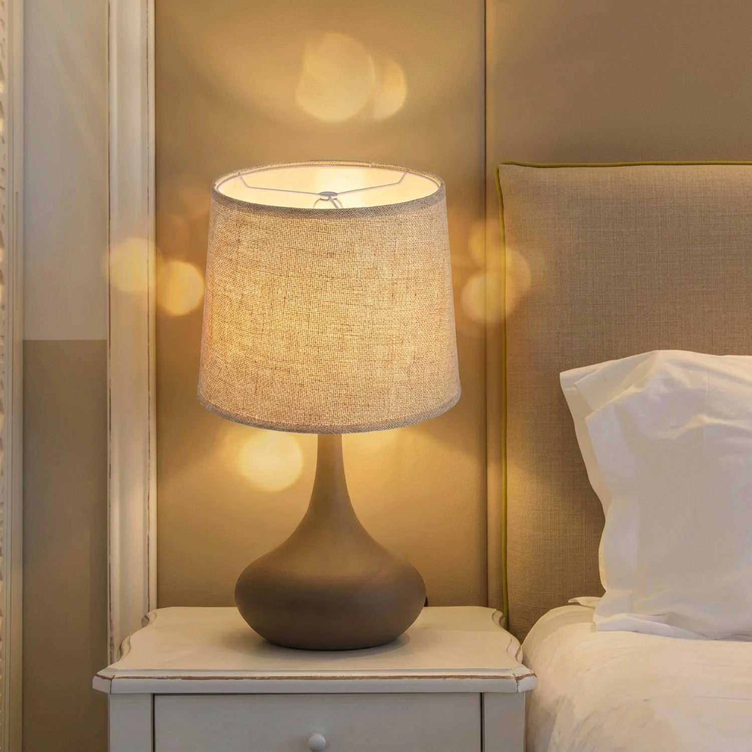Abat-jour tambour en tissu lin beige allumé sur lampe de table dans un salon chaleureux