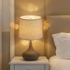 Abat-jour tambour en tissu lin beige allumé sur lampe de table dans un salon chaleureux