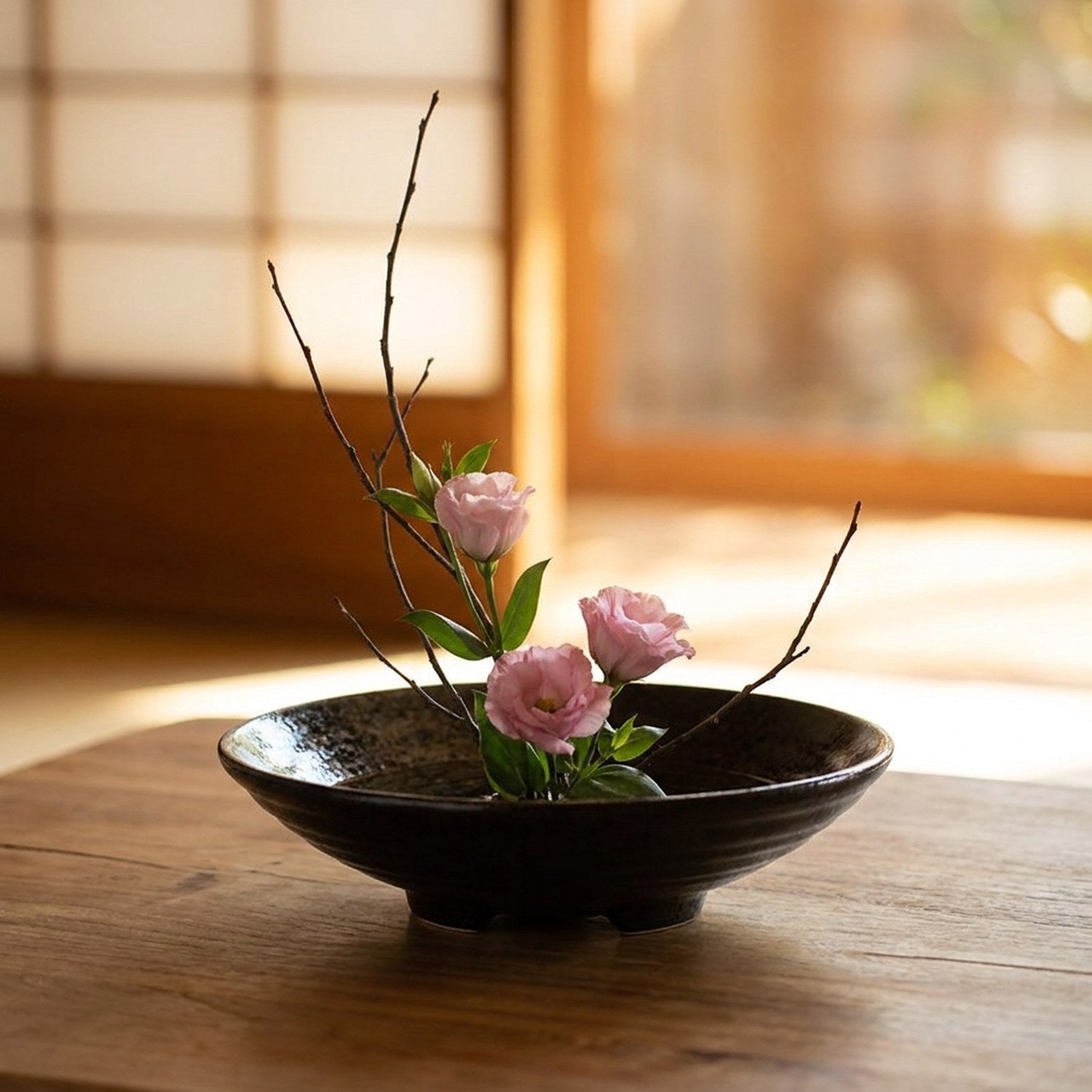 Vase japonais en céramique noire posé sur une table avec une composition florale ikebana