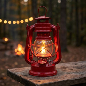 Lampe à pétrole vintage rouge en métal allumée sur une table en bois en extérieur