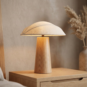 Lampe de chevet champignon en bois avec abat-jour en lin allumée diffusant une lumière chaude sur une table de nuit