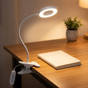 Lampe de bureau blanche à pince avec bras flexible col de cygne et anneau LED allumé sur un bureau en bois