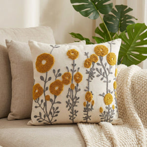 Housse de coussin carrée brodée de fleurs moutarde sur fond écru posée sur un canapé