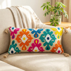 housse de coussin lombaire brodée aux motifs floraux colorés avec pompons posée sur un canapé en lin