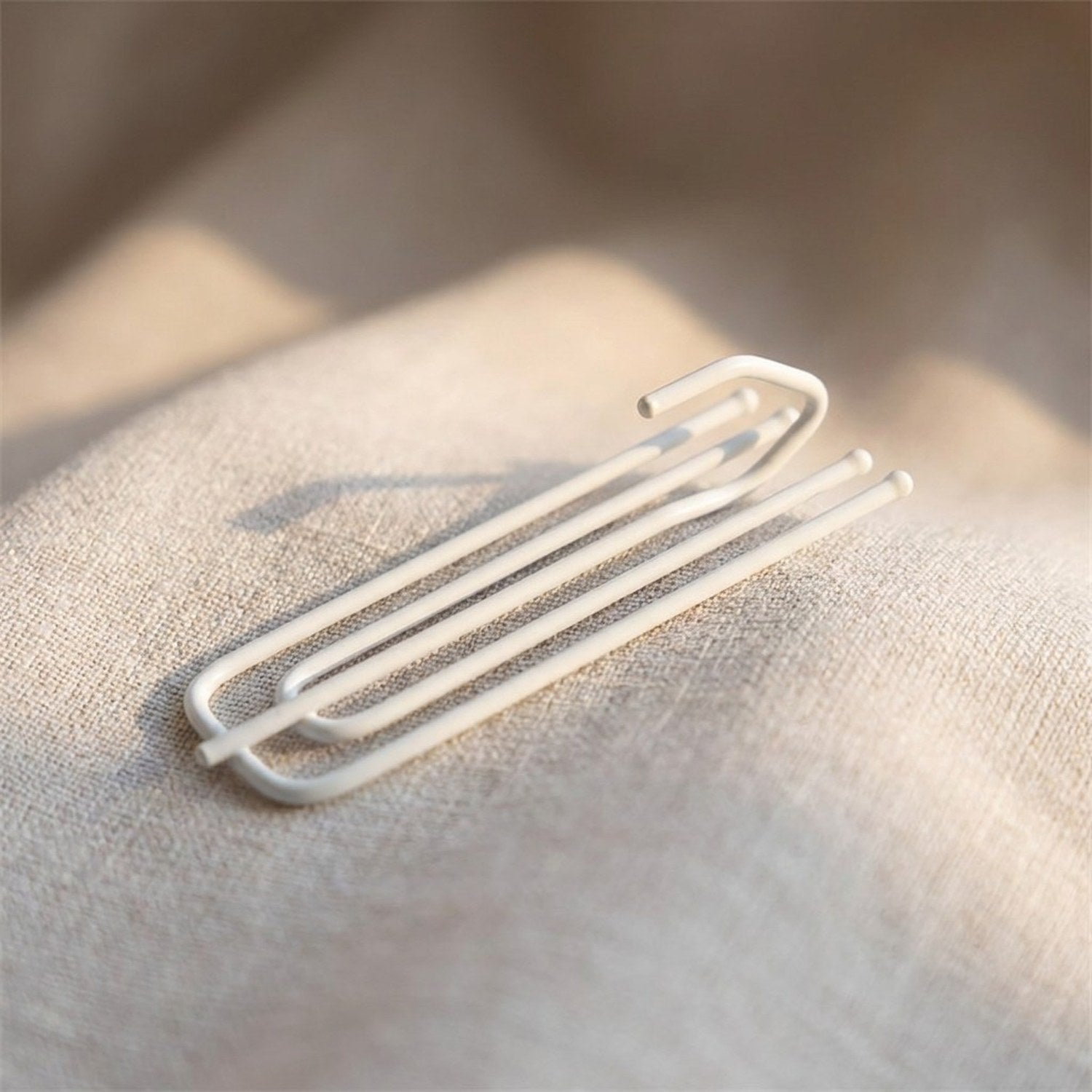 Crochet de rideau blanc à quatre broches métalliques posé sur un tissu en lin clair