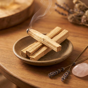 Bâtonnets de Palo Santo en bois clair fumant dans une coupelle en céramique sur une table en bois