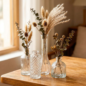 Collection de vases en verre vintage transparents au relief ciselé garnis de fleurs séchées sur une table en bois