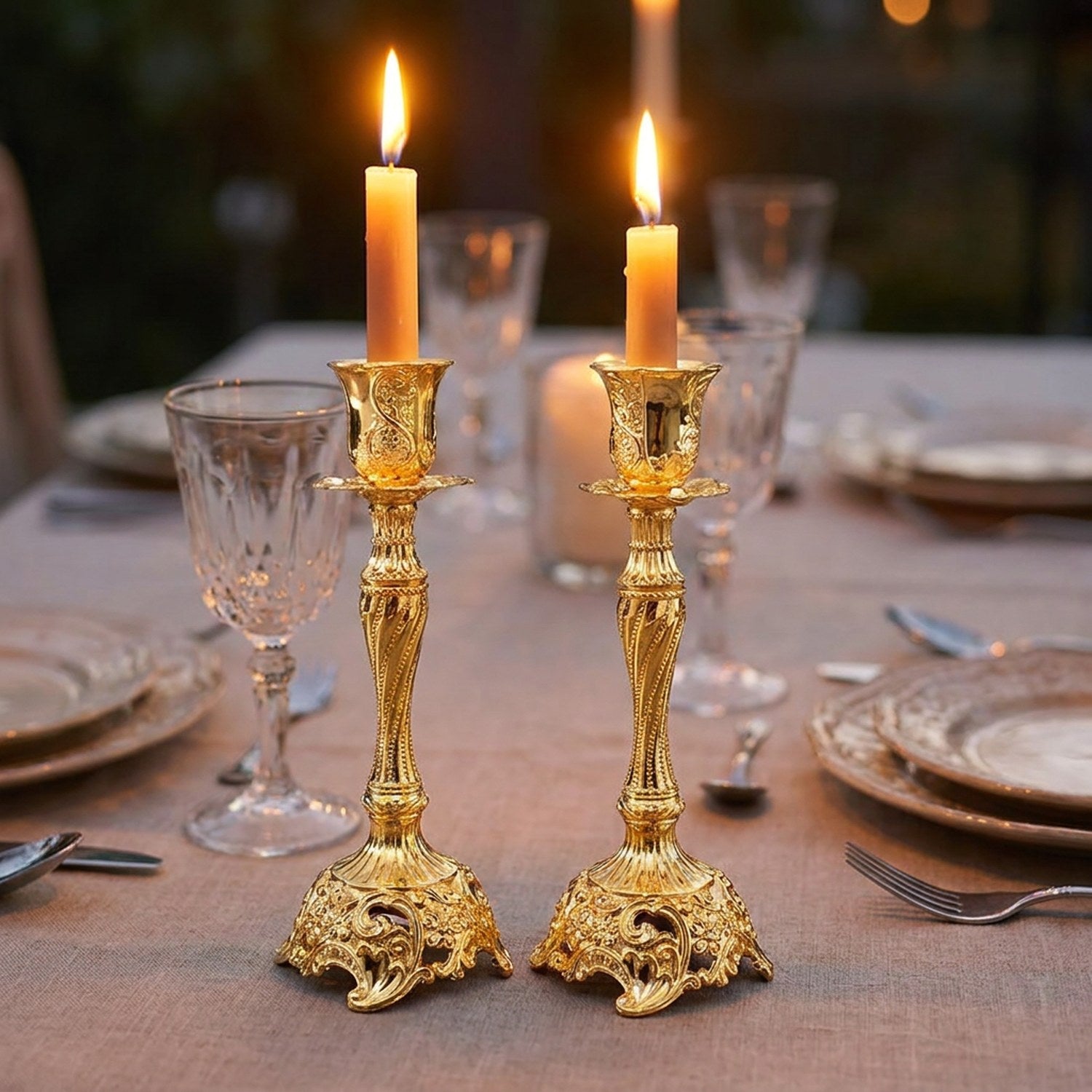 Lot de deux bougeoirs en métal doré au style baroque avec bougies allumées sur une table de fête