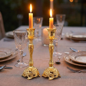 Lot de deux bougeoirs en métal doré au style baroque avec bougies allumées sur une table de fête
