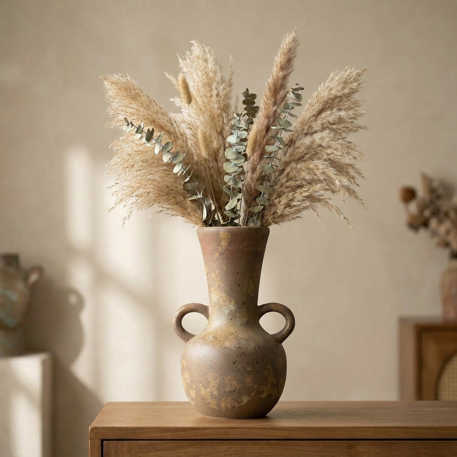 Vase grec en céramique rustique à anses garni de pampa séchée sur une console en bois