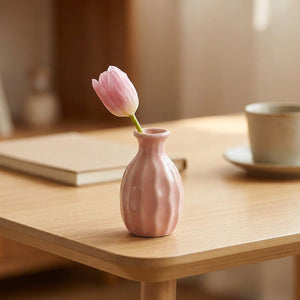 Vase soliflore en céramique côtelé rose avec une fleur unique sur un bureau