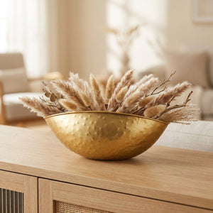 Coupe décorative en métal doré martelé de forme bateau garnie de pampas posée sur une console