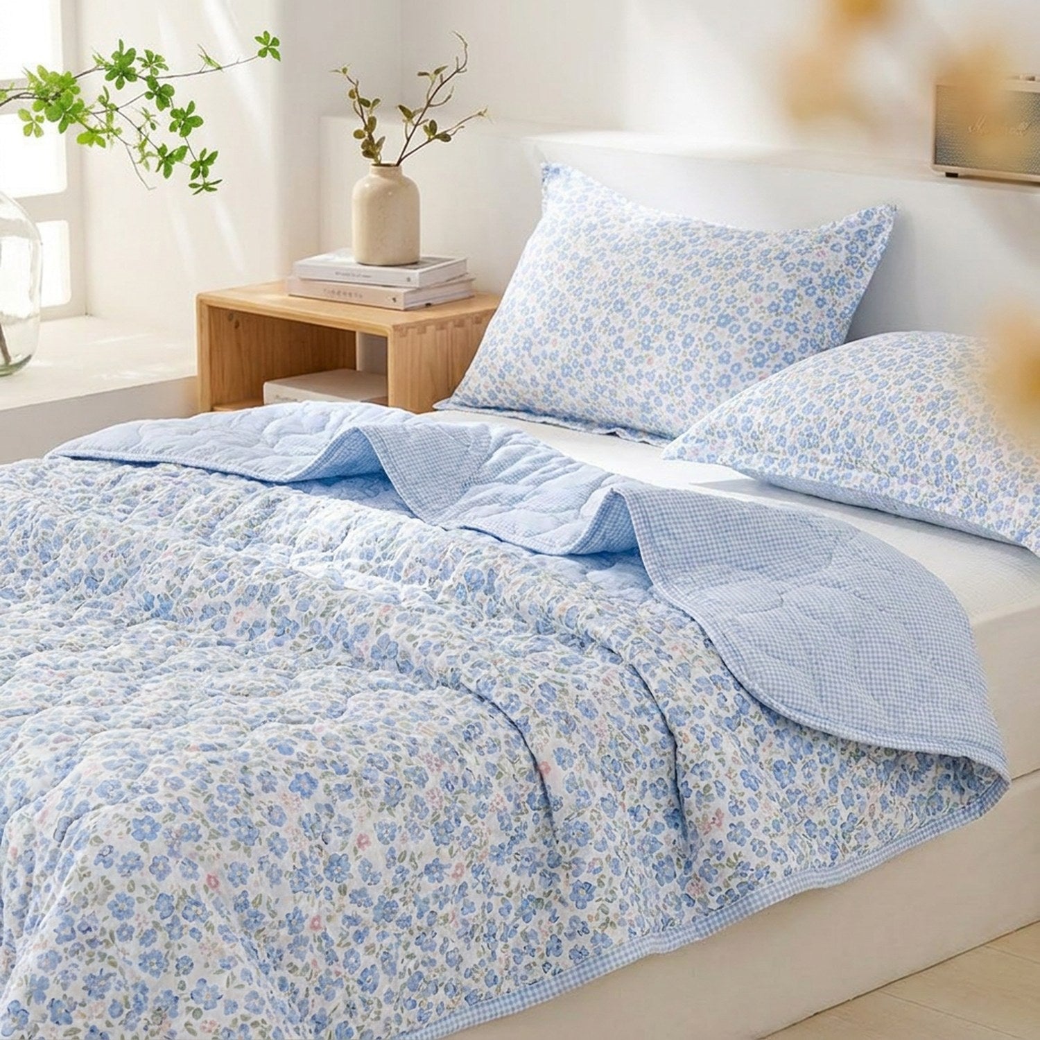 Couette d'été matelassée bleue à motif floral posée sur un lit dans une chambre lumineuse avec deux taies assorties