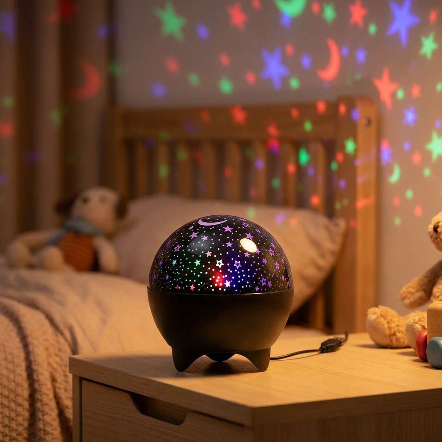 Veilleuse projecteur ciel étoilé noire allumée sur une table de chevet projetant des étoiles colorées dans une chambre d'enfant