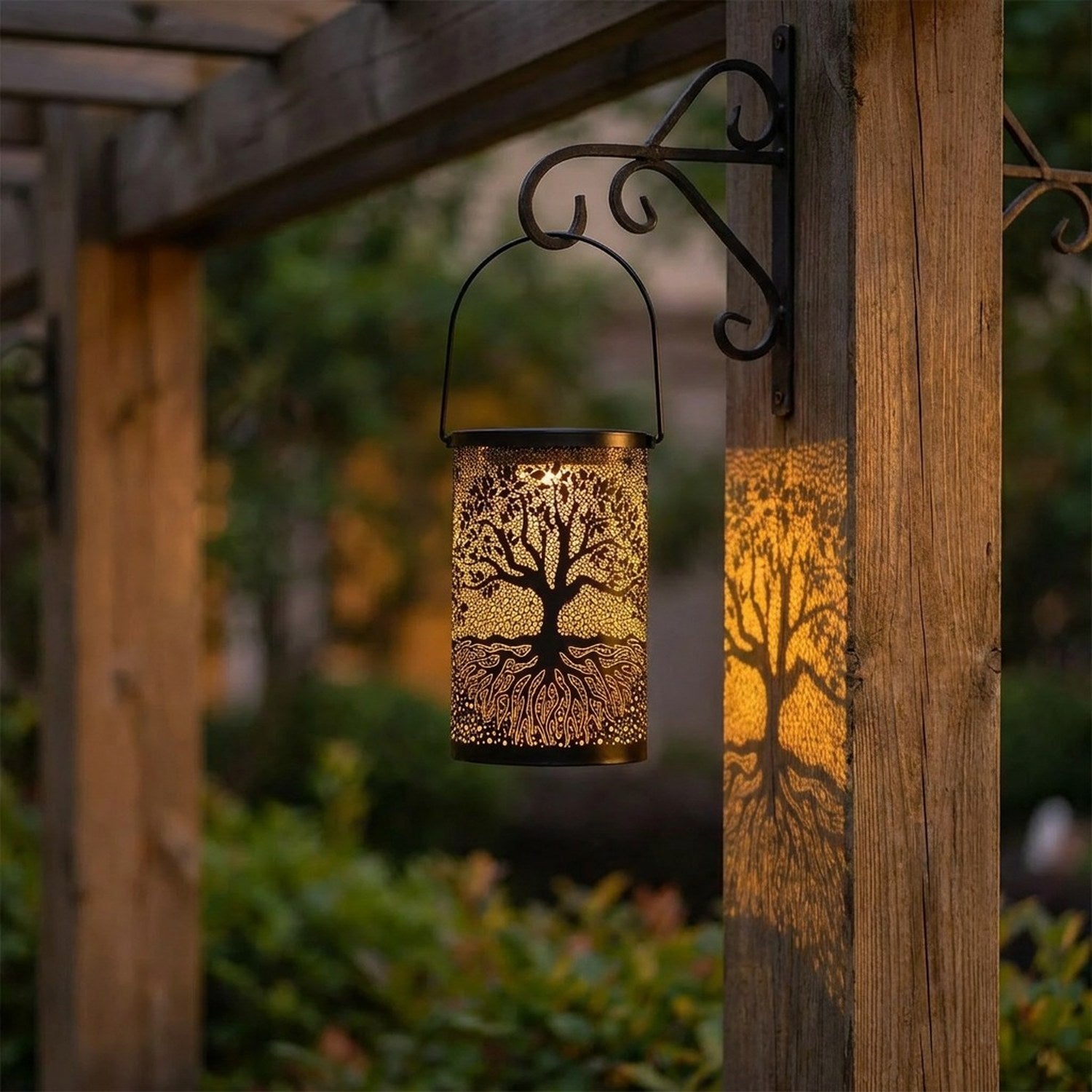 Lanterne solaire en métal noir ajouré motif arbre de vie suspendue dans un jardin la nuit