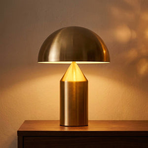 Lampe de table champignon en métal doré allumée posée sur une console en bois dans un salon nordique