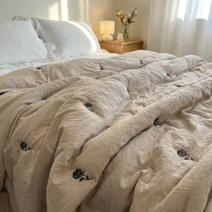 Couette d'été en coton lavé beige brodée de roses posée sur un lit dans une chambre douce