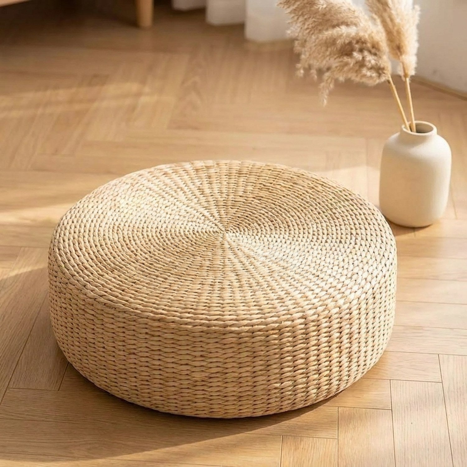 Pouf rond en paille tressée naturelle posé sur un parquet clair dans une ambiance zen