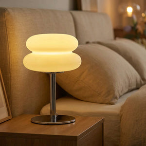 Lampe de chevet champignon en verre blanc dépoli allumée sur une table de nuit en bois