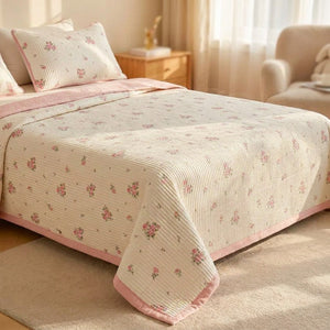 Couvre-lit matelassé motifs floraux roses posé sur un lit fait dans une chambre lumineuse