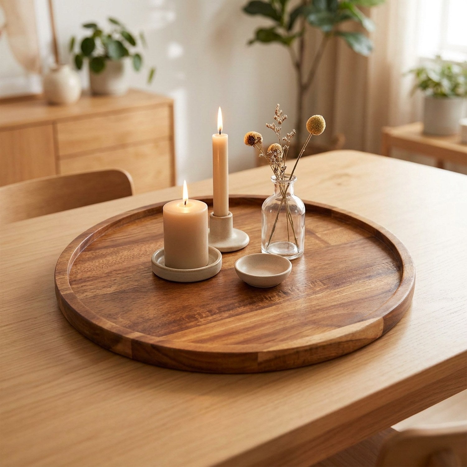 Plateau rond en bois d'acacia garni de bougies et de fleurs séchées sur une table claire