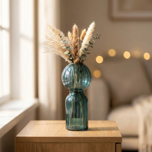 Vase en verre nervuré bleu posé sur une table claire avec quelques branchages dans une lumière douce