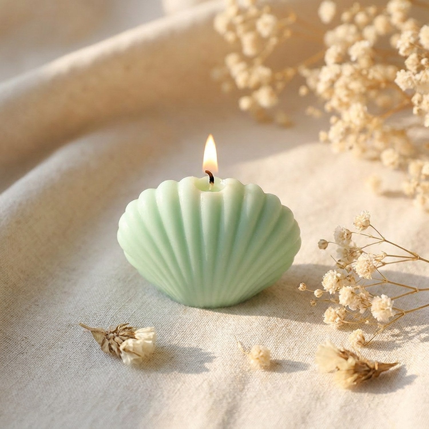 Bougie parfumée en forme de coquillage vert menthe allumée sur du lin avec des fleurs séchées