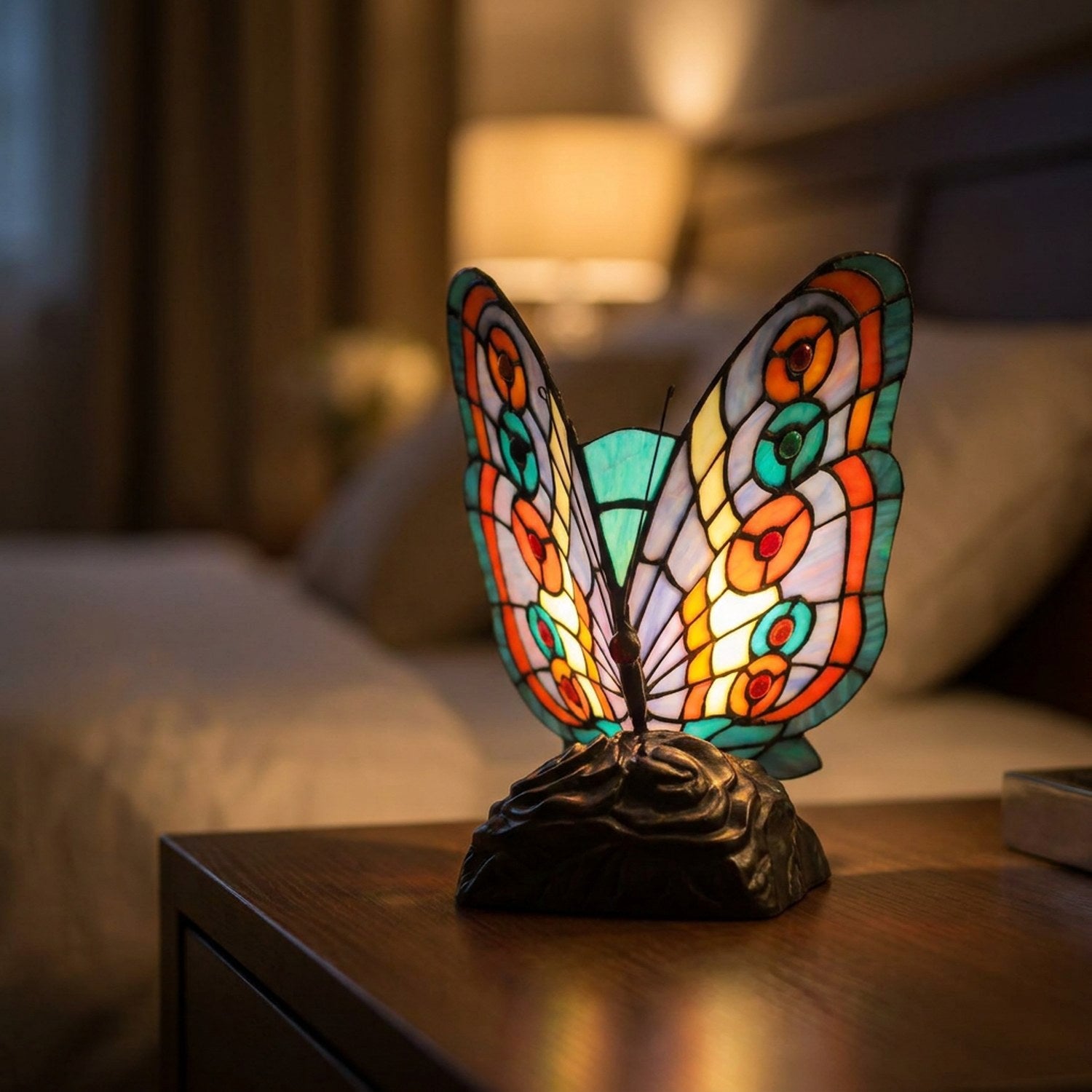 Lampe style Tiffany en forme de papillon en vitrail multicolore allumée posée sur une table de chevet en bois
