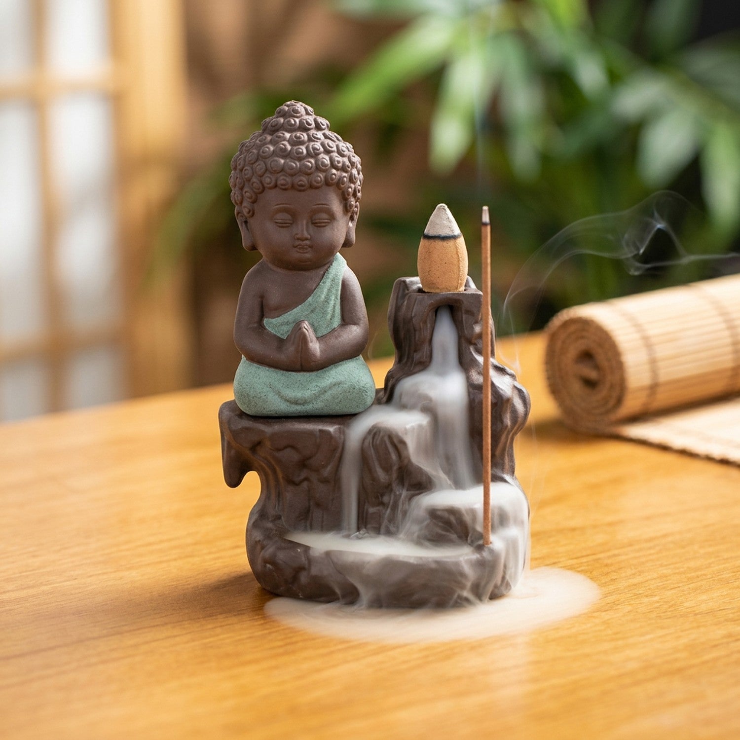 Brûleur d'encens à reflux en céramique avec petit moine bouddha à la robe verte et fumée qui cascade sur une table en bois