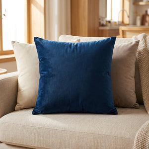 Housse de coussin en velours bleu marine posée sur un canapé clair dans un salon chaleureux