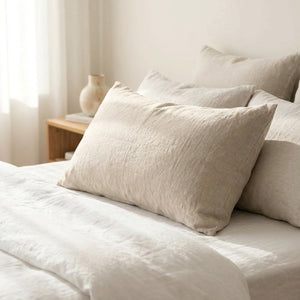 Taie d'oreiller en lin lavé beige posée sur un lit dans une chambre lumineuse et apaisante
