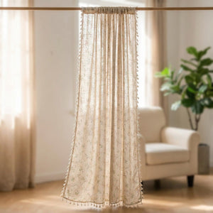 Rideau boho floral en lin et coton à pompons suspendu devant une fenêtre lumineuse