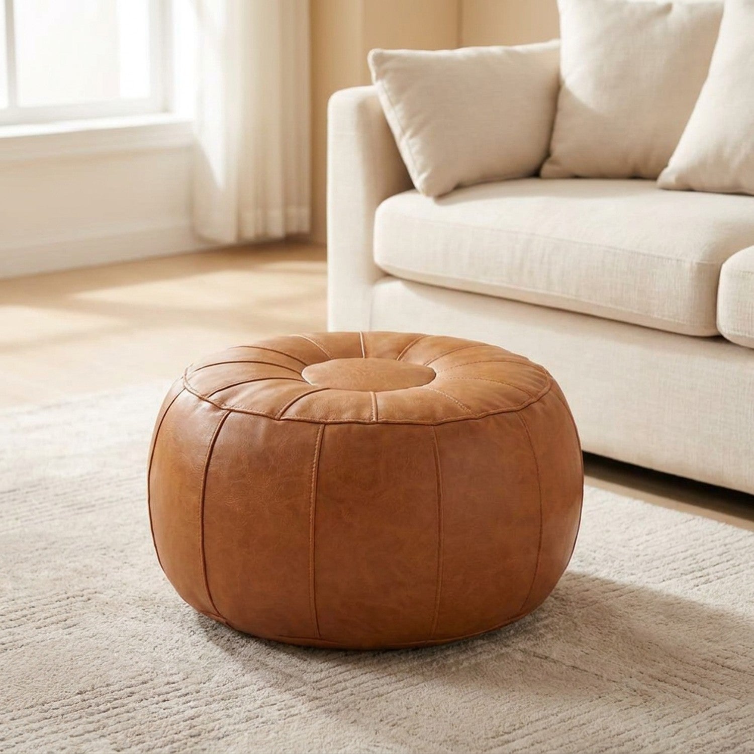 Pouf de rangement rond en simili cuir caramel style marocain posé devant un canapé blanc