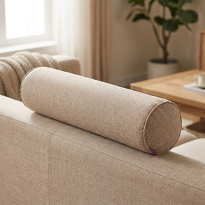 Housse de traversin cylindrique beige posée sur le dossier d'un canapé en lin