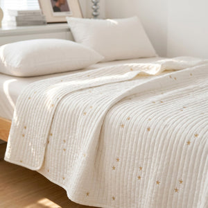 Couvre-lit matelassé blanc brodé d'étoiles dorées posé sur un lit avec coussins