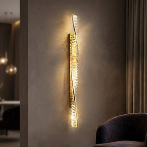 Applique murale LED cristal et métal doré au design torsadé allumée sur un mur élégant