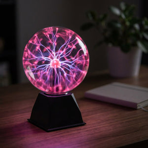 Lampe boule plasma allumée avec des arcs électriques roses et violets posée sur un bureau sombre