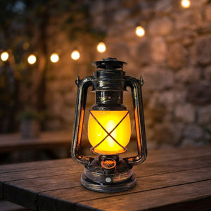 Lanterne vintage en métal finition bronze avec verre orangé façon flamme posée sur une table en bois