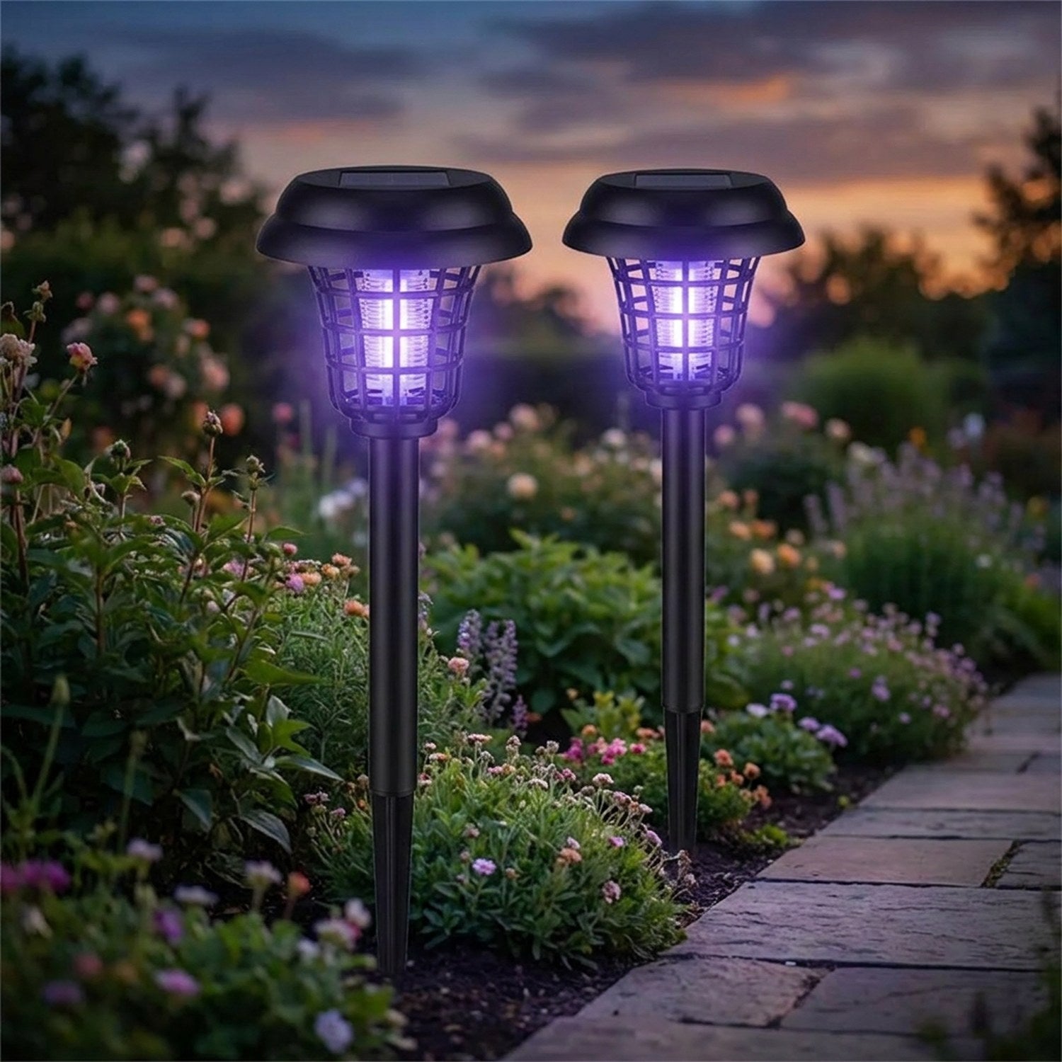 Deux lampes anti moustique solaires noires plantées dans un massif de jardin éclairées d'une lumière violette au crépuscule
