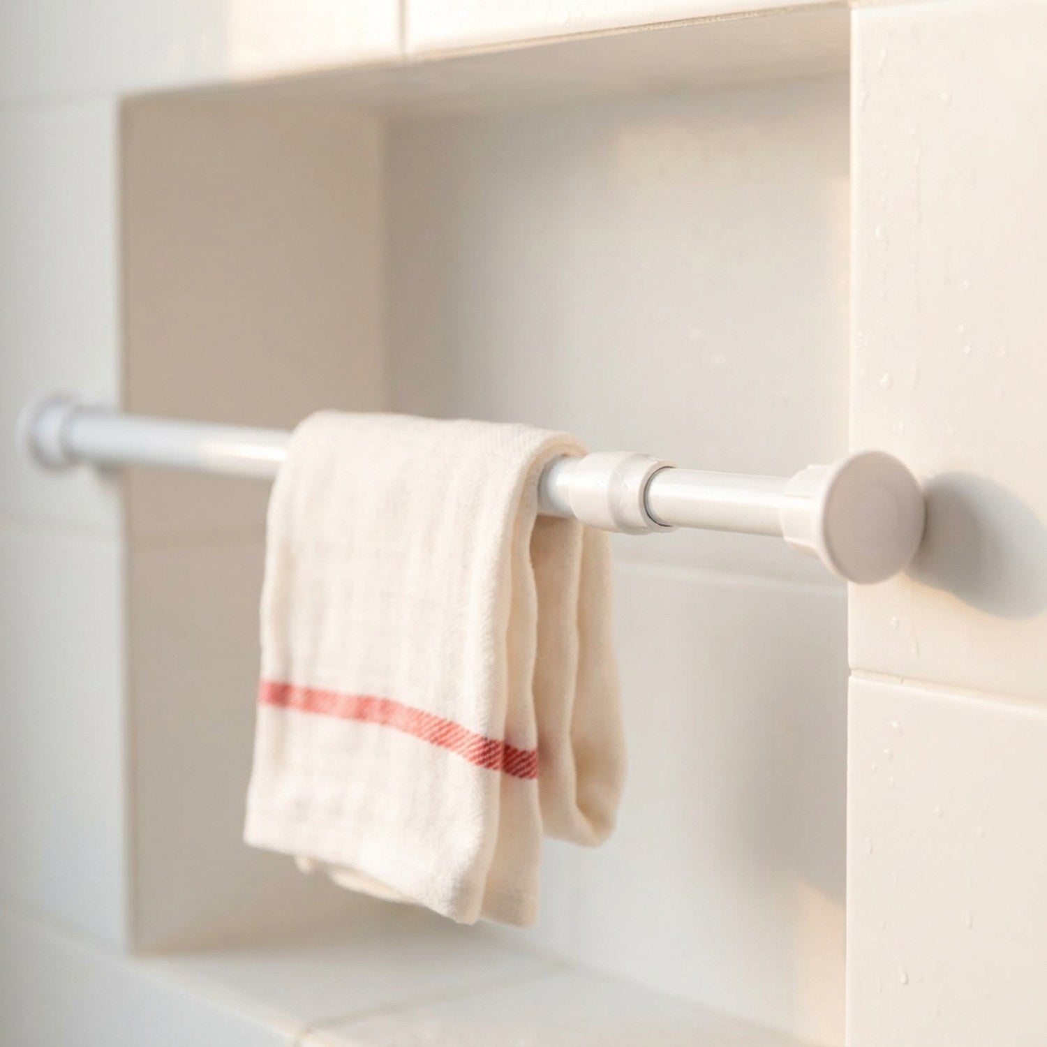 Tringle extensible blanche fine installée dans une niche de douche carrelée