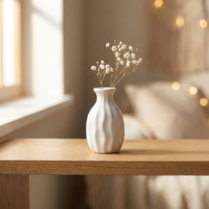 Vase miniature en céramique blanche avec une fleur séchée sur une table en bois