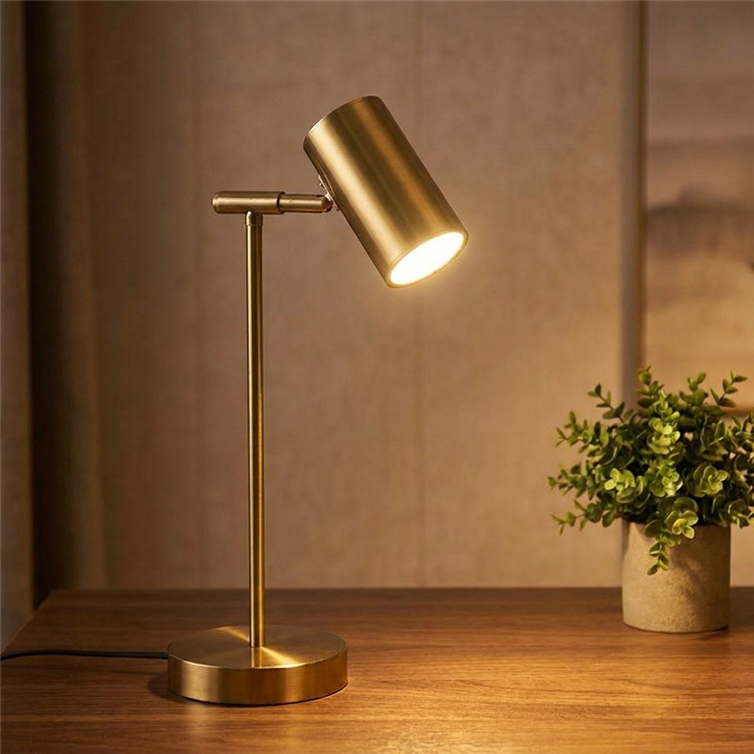 Lampe de bureau dorée à tête cylindrique orientable allumée posée sur un bureau en bois