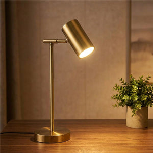 Lampe de bureau dorée à tête cylindrique orientable allumée posée sur un bureau en bois
