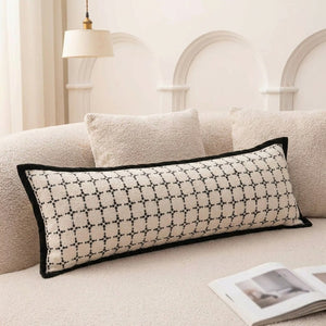 Traversin rectangulaire écru à motifs graphiques noirs posé sur un canapé en bouclette beige
