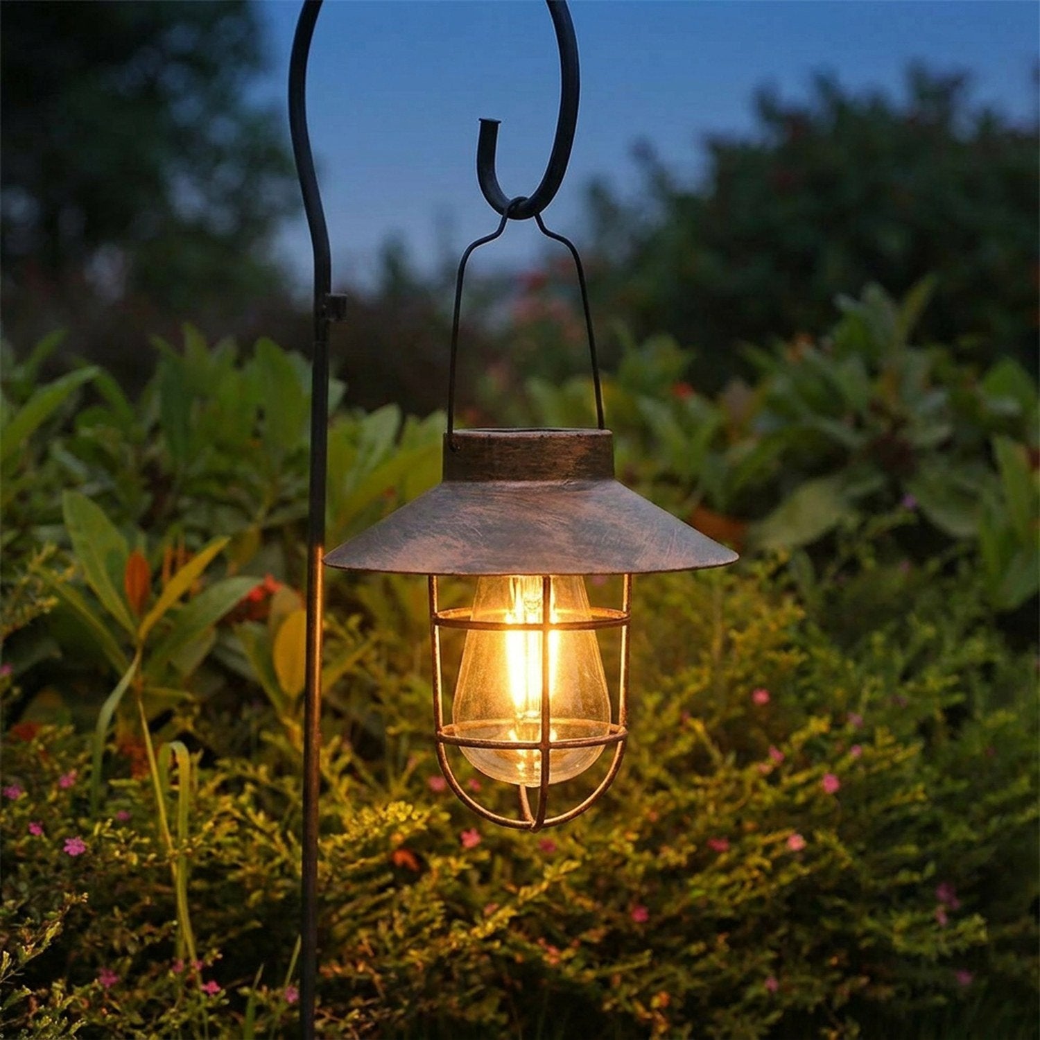Lanterne solaire extérieure rétro en métal bronze avec ampoule LED allumée suspendue dans un jardin au crépuscule