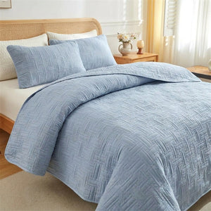 Couvre-lit matelassé tressé bleu sur un lit fait avec deux taies d'oreiller dans une chambre lumineuse