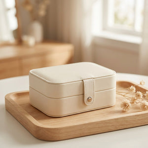 Boîte à bijoux de voyage en simili cuir crème posée sur un plateau en bois