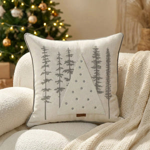 Housse de coussin brodée de sapins gris sur un fauteuil avec sapin de Noël en arrière-plan