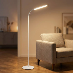 Lampadaire LED blanc à col de cygne orientable allumé à côté d'un fauteuil dans un salon